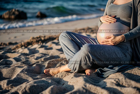 Relaxation, peace of mind, sea air. Close-up of the tummy. A pregnant woman on the beach by the sea. The concept of pregnancy, childbirth and parental responsibilities. Стоковое AI-изображение, AI-художник Photojuli / Фотобанк Лори