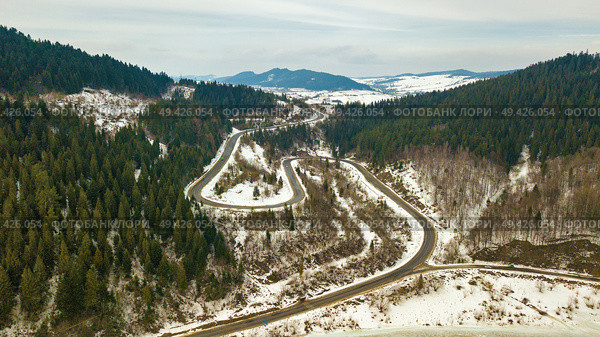Road serpentine in winter snowy mountain landscape. Aerial rural view of road passing to horizon. Carpathian mountains, Beskids range. Стоковое фото, агентство Ingram Publishing / Фотобанк Лори