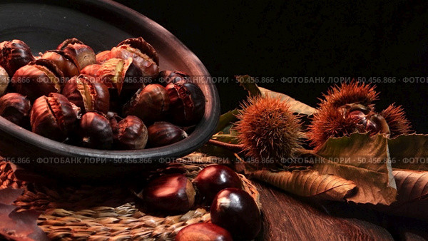 Roasted chestnuts on a rustic wooden table with autumn leaves in the background. Стоковое фото, агентство Ingram Publishing / Фотобанк Лори