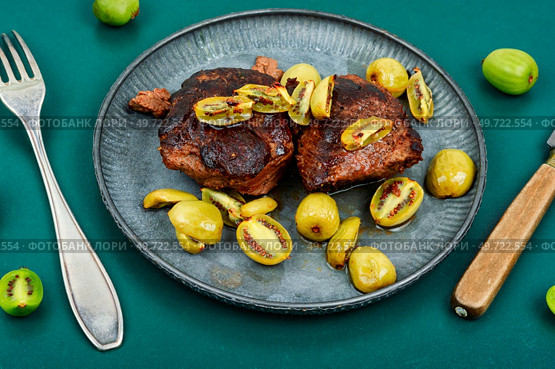 Roasted ostrich steak and mini kiwi on a plate. Grilled ostrich steak with kiwi berries. Стоковое фото, агентство Ingram Publishing / Фотобанк Лори