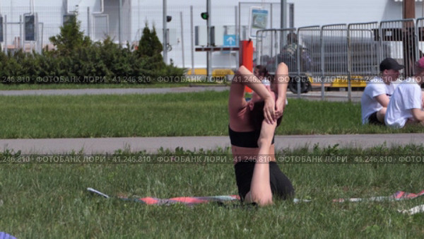 Russia, Nizhny Novgorod, VUO, Volga embankment 43 06.05.2021. A young woman is doing yoga on the street, in a beautiful meadow in summer. High quality FullHD footage. Редакционное видео, видеограф Egor Sarantstv / Фотобанк Лори