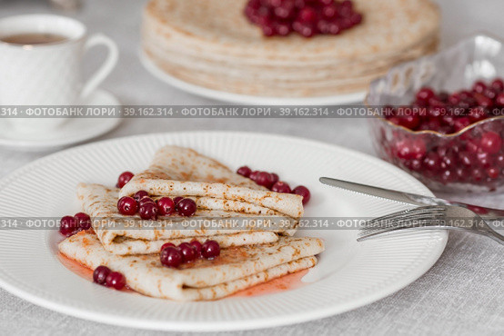 Russian traditions. Russian holiday Maslenitsa. Still life with a cup of tea, a stack of pancakes with northern cranberries, cubes of butter on the table. Стоковое фото, фотограф Photojuli / Фотобанк Лори