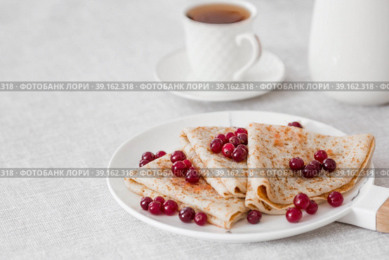 Russian traditions. Russian holiday Maslenitsa. Still life with a cup of tea, a stack of pancakes with northern cranberries, cubes of butter on the table. Стоковое фото, фотограф Photojuli / Фотобанк Лори
