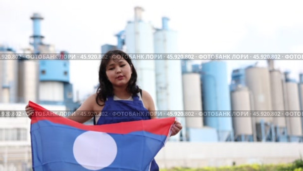 Sad young woman holding big flag of Laos against background of factory. Стоковое видео, видеограф Яков Филимонов / Фотобанк Лори