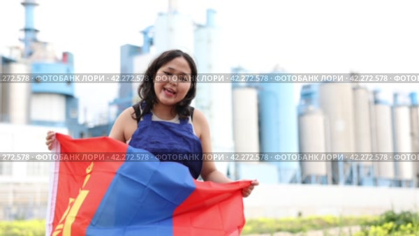 Sad young woman holding big flag of Mongolia against background of factory. Стоковое видео, видеограф Яков Филимонов / Фотобанк Лори