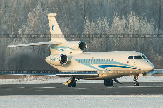 Самолет (бизнес джет) Dassault Falcon 7X авиакомпании Газпром Авиа на рулении в аэропорту Пулково зимой, на фоне покрытого белым инеем леса (2019 год). Редакционное фото, фотограф Сергей Крамарев / Фотобанк Лори