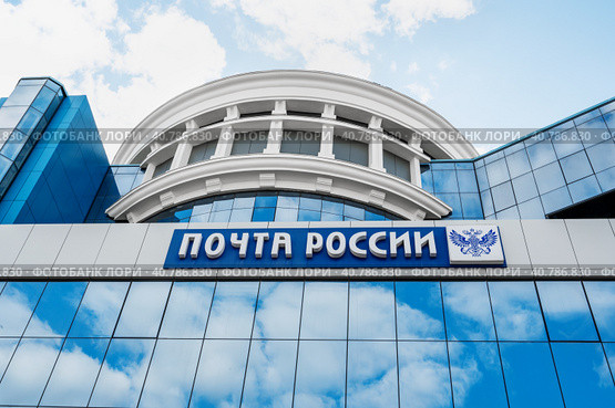 Saransk, Mordovia, Russia, 4.06.2023. The blue facade of the building with the inscription Russian Post and a double-headed Russian eagle, against the background of the reflection of clouds on the glass surface. Редакционное фото, фотограф Оксана Медведева / Фотобанк Лори