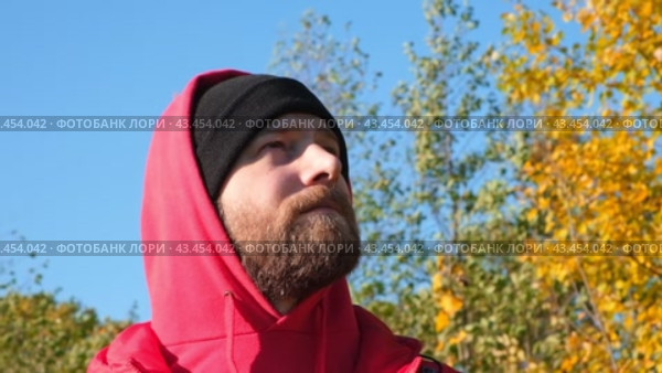 Satisfied Traveler Guy Wearing Red Hoody Stands in Picturesque Place of Wildlife, Looks Up at Autumn Landscape. Concept People Traveling and Success. Low Angle Shot of 30s Man in Fall Nature Closeup. Стоковое видео, видеограф Марина Демидюк / Фотобанк Лори