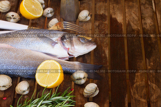 Seabass. Two Seabass raw fish with shellfish and spices on wooden table  w. Стоковое фото, агентство Ingram Publishing / Фотобанк Лори