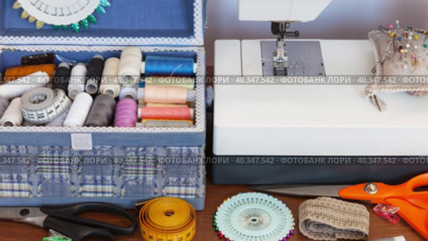 Seamstress workplace at home. Sewing machine, blue box with sewing supplies, accessories: skeins of colorful threads, pins, needles, measuring tape on wooden table. Needlework, craft, DIY concept. Стоковое видео, видеограф Виктория Катьянова / Фотобанк Лори