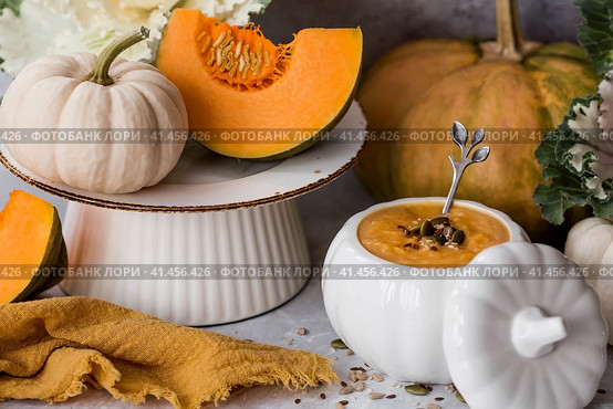 Seasonal autumn food. Traditional pumpkin cream soup in a pumpkin-shaped bowl and fresh pumpkin on a gray marble background. Стоковое фото, фотограф Photojuli / Фотобанк Лори