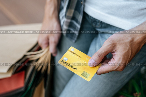 Select focus credit card in hand of Young handsome man in mask, He holding paper bag and show credit card on stair of shopping mall, New normal lifestyle and shopping concept, copy space. Стоковое фото, агентство Ingram Publishing / Фотобанк Лори