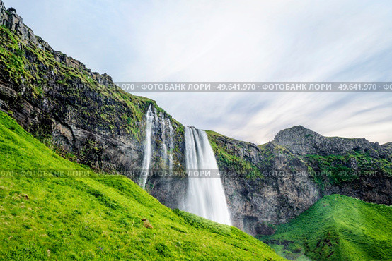 Seljalandsfoss waterfalls in Iceland with green hills and lava cliffs. Стоковое фото, агентство Ingram Publishing / Фотобанк Лори