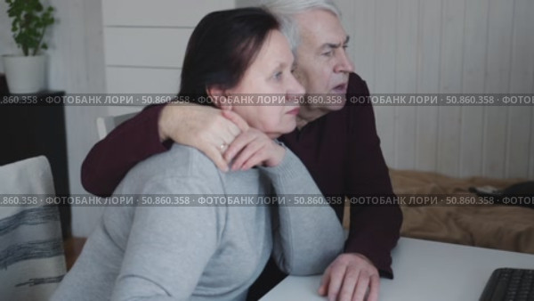 Senior couple using laptop together in the room. Embracing elderly man and woman reading email or online shopping choice. Old man and woman talk at table in home together on internet, social media. 4K. Стоковое видео, видеограф Марина Демидюк / Фотобанк Лори