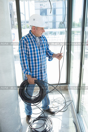 senior electrician holding reel of cable at indoor work site. Стоковое фото, агентство Ingram Publishing / Фотобанк Лори