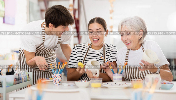 Senior woman assisting happy guy and girl painting ceramic mugs in workshop. Стоковое фото, фотограф Яков Филимонов / Фотобанк Лори
