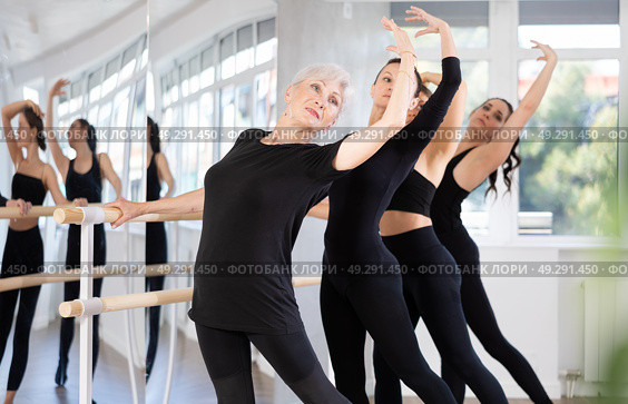 Senior woman performing battement tendu at barre during group rehearsal. Стоковое фото, фотограф Яков Филимонов / Фотобанк Лори
