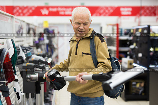 Senor man pensioner buying Upright Vacuum Cleaner in showroom of electrical appliance store. Стоковое фото, фотограф Татьяна Яцевич / Фотобанк Лори