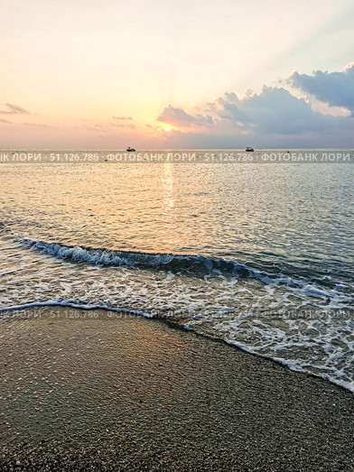 Serene beach at sunrise with gentle waves lapping against the shore and colorful sky reflections. Стоковое фото, фотограф Наталья Семкина / Фотобанк Лори