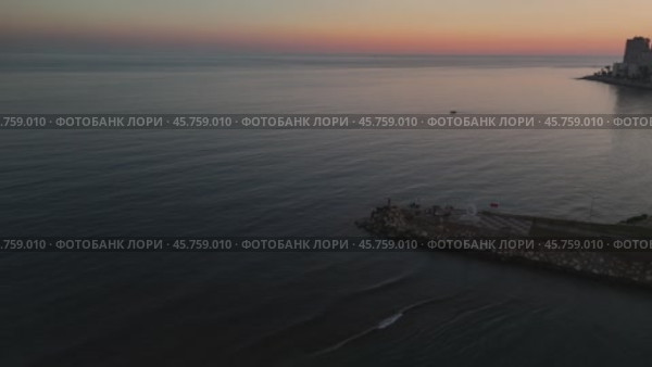 Serene sea mirroring sunset hues, small boat nearing mersin coastline, silhouetted figures standing on weathered wooden pier during twilight. Стоковое видео, видеограф ILIA GOROKHOV / Фотобанк Лори