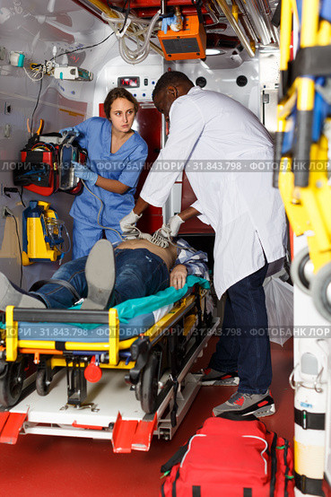 serious afro paramedical using defibrillator for providing medical care to patient. Стоковое фото, фотограф Яков Филимонов / Фотобанк Лори