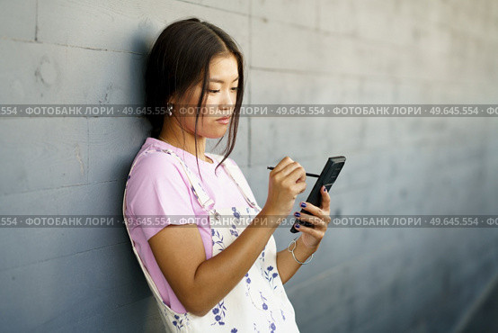 Serious Chinese girl using her smartphone with a pen or stylus,outdoors Asian female wearing casual clothes.. Serious Chinese girl using her smartphone with a pen or stylus,outdoors. Стоковое фото, агентство Ingram Publishing / Фотобанк Лори