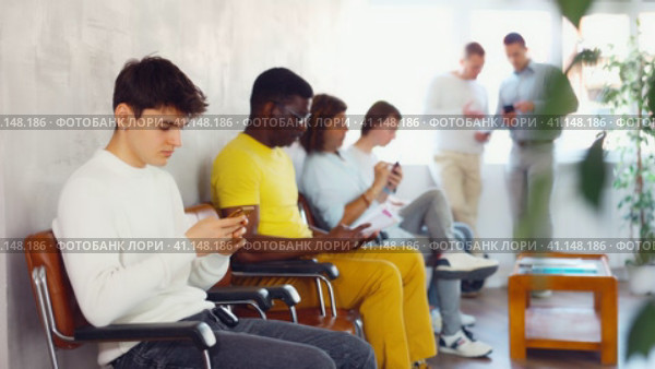 Serious man browsing websites on smartphone while sitting in lobby of job center or employment office, waiting for interview or conversation with career counselor. Стоковое видео, видеограф Яков Филимонов / Фотобанк Лори