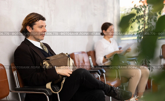 Serious-minded male candidate siting on chair and waiting for job interview in hallway. Стоковое фото, фотограф Яков Филимонов / Фотобанк Лори