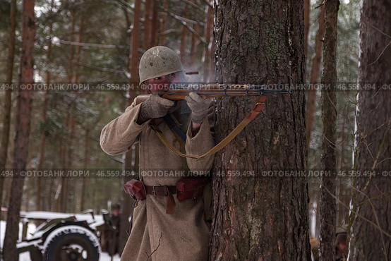 Sestroretsk, Russia - February 19, 2023: Capturing the essence of a winter battlefield, a soldier takes cover behind a tree, engaged in combat. Редакционное фото, фотограф Aleksandr Golubev / Фотобанк Лори