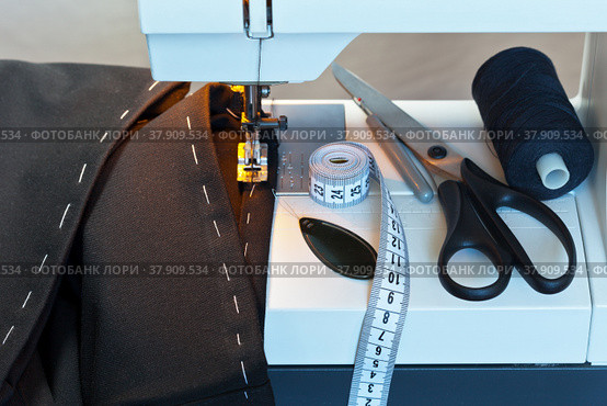 Sew at home. Processing the bottom of the  trousers on the sewing machine. Sewing accessories: black thread, needle threader, scissors and measuring tape. Стоковое фото, фотограф Виктория Катьянова / Фотобанк Лори