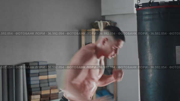 Shirtless sweaty young man boxer punching the punching bag. Стоковое видео, видеограф Константин Шишкин / Фотобанк Лори