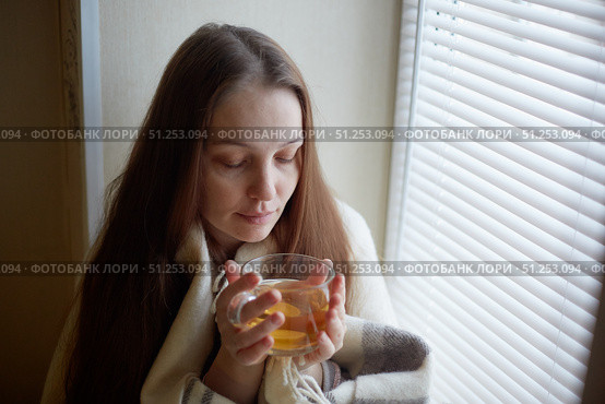 sick beautiful woman with colds and drinks hot tea with lemon sitting by the window in a country house in winter. Стоковое фото, фотограф Арзюков Вадим Николаевич / Фотобанк Лори