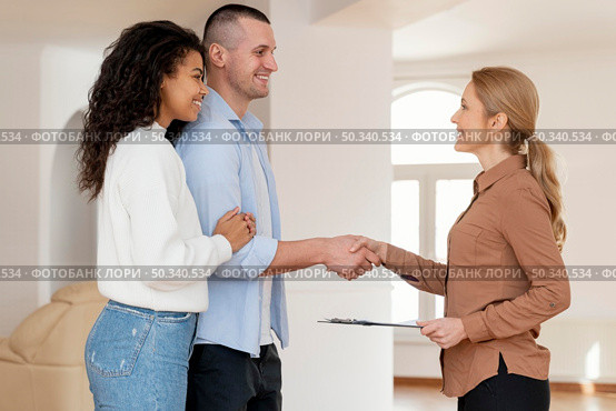 side view female realtor shaking hands with couple new house deal. Стоковое фото, агентство Ingram Publishing / Фотобанк Лори