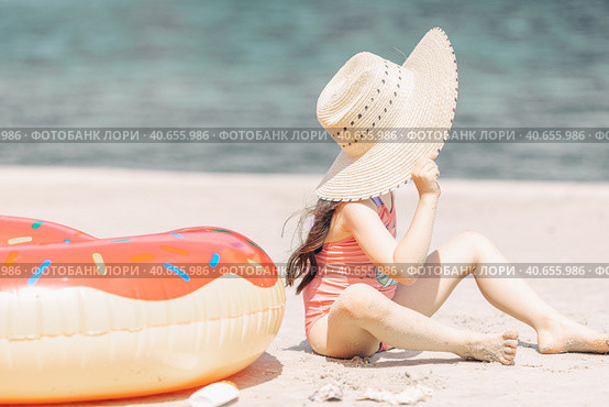 Side view of cute little girl sitting on the sand on a beach in a swimsuit and straw hat. Стоковое фото, фотограф Ирина Михайличенко / Фотобанк Лори
