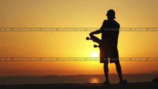 Silhouette of a man standing near the ocean holding a longboard at bright orange sunset. Стоковое видео, видеограф Константин Шишкин / Фотобанк Лори