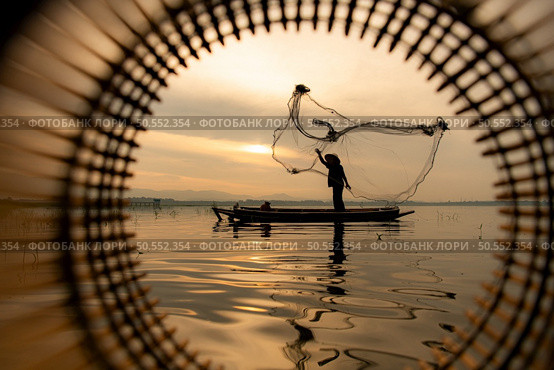Silhouette of fisherman at sunrise, Standing aboard a rowing boat and casting a net to catch fish for food. Стоковое фото, агентство Ingram Publishing / Фотобанк Лори
