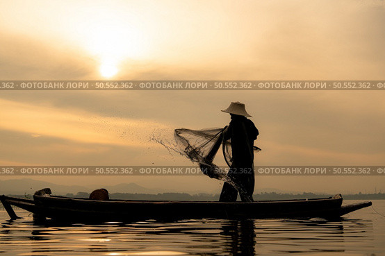 Silhouette of fisherman at sunrise, Standing aboard a rowing boat and casting a net to catch fish for food. Стоковое фото, агентство Ingram Publishing / Фотобанк Лори