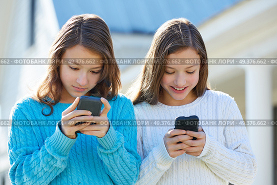 Sister twins having fun with technology mobile smartphone. Стоковое фото, агентство Ingram Publishing / Фотобанк Лори