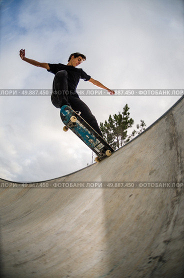 Skateboarder doing a tail slide on a croncrete pool at the skate park. Стоковое фото, агентство Ingram Publishing / Фотобанк Лори