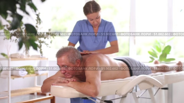 Skilled middle-aged masseuse conducting back massage therapy for man client in procedure room. Стоковое видео, видеограф Яков Филимонов / Фотобанк Лори