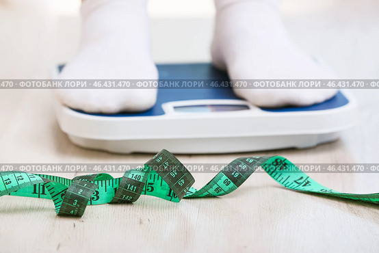 Skinny woman with measuring tape standing on floor scales. Concept of anorexia. Стоковое фото, фотограф Pixel_shot / Фотобанк Лори