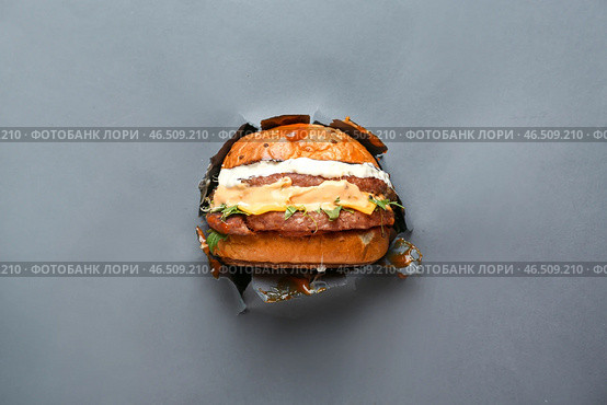 Сквозь дыру в рваной бумаге виден вкусный бургер. Стоковое фото, фотограф Pixel_shot / Фотобанк Лори