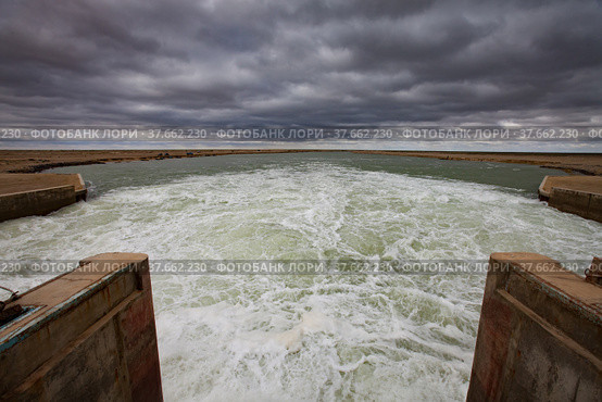 Small Aral Sea Kok-aral dam. Kazakhstan, Kyzylorda region. Concrete supports, metal shutters. turbulent water after dam.Grey storm sky. Стоковое фото, фотограф Alexey Rezvykh / Фотобанк Лори