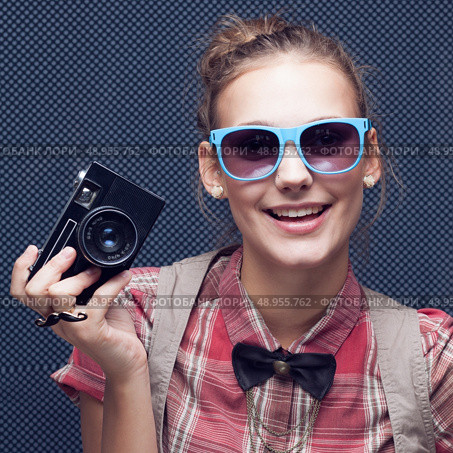 Smiling hipster girl with vintage camera. Trendy teenager in checkered red shirt and bow-tie and sunglasses. Стоковое фото, агентство Ingram Publishing / Фотобанк Лори
