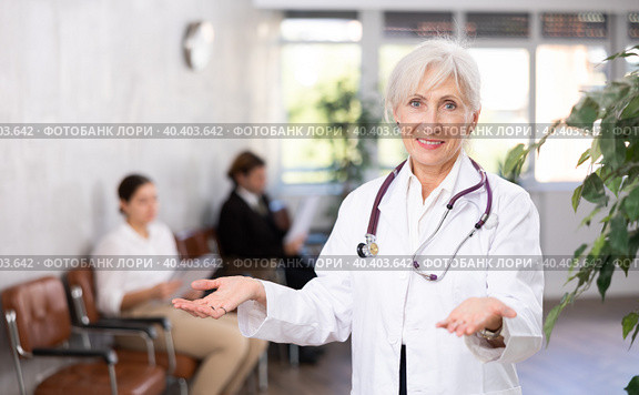 smiling mature medical female receptionist affably waiting for patients of clinic in waiting room. Стоковое фото, фотограф Яков Филимонов / Фотобанк Лори