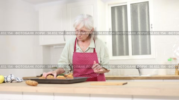 Smiling senior woman putting hot just prepared cupcakes on kitchen table. Стоковое видео, видеограф Яков Филимонов / Фотобанк Лори