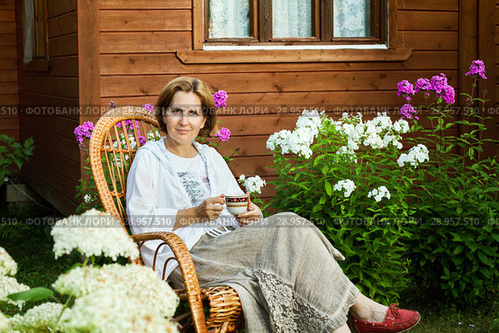 Smiling woman is resting in a wicker chair at a summer cottage in the evening. Стоковое фото, фотограф Юлия Кузнецова / Фотобанк Лори