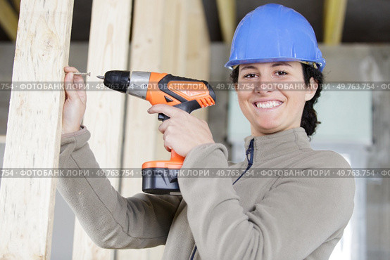smiling young professional woman using cordless screwdriver on wood. Стоковое фото, агентство Ingram Publishing / Фотобанк Лори