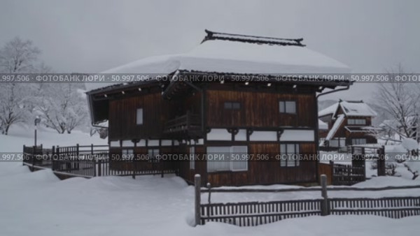 Snow covers the roof and surroundings of a traditional japanese wooden house with a wooden fence in a winter landscape, evoking a sense of tranquility and peace. Стоковое AI-видео, аниматор Данил Руденко / Фотобанк Лори