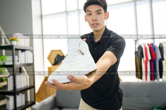 Social media influencer reviewing fashion shoe. Smiling young man vlogging about men’s sports shoe and filming himself at home on a video camera. Стоковое фото, агентство Ingram Publishing / Фотобанк Лори